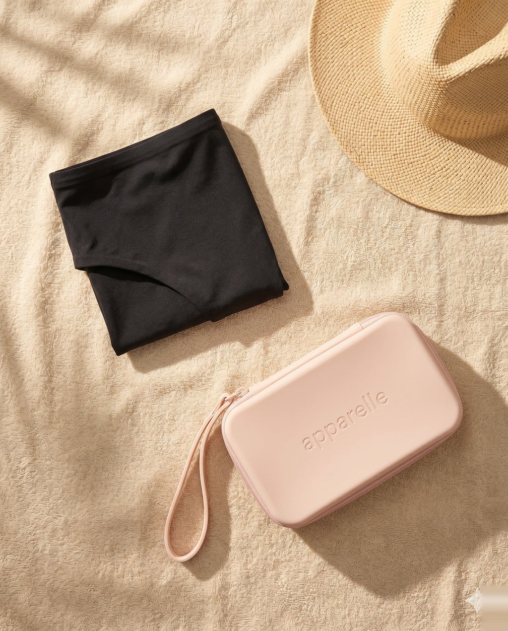 Bikini menstrual Apparelle doblado sobre toalla junto al Neceser Waterproof rosa — kit listo para llevar una segunda unidad y mantenerla aislada del bañador mojado.