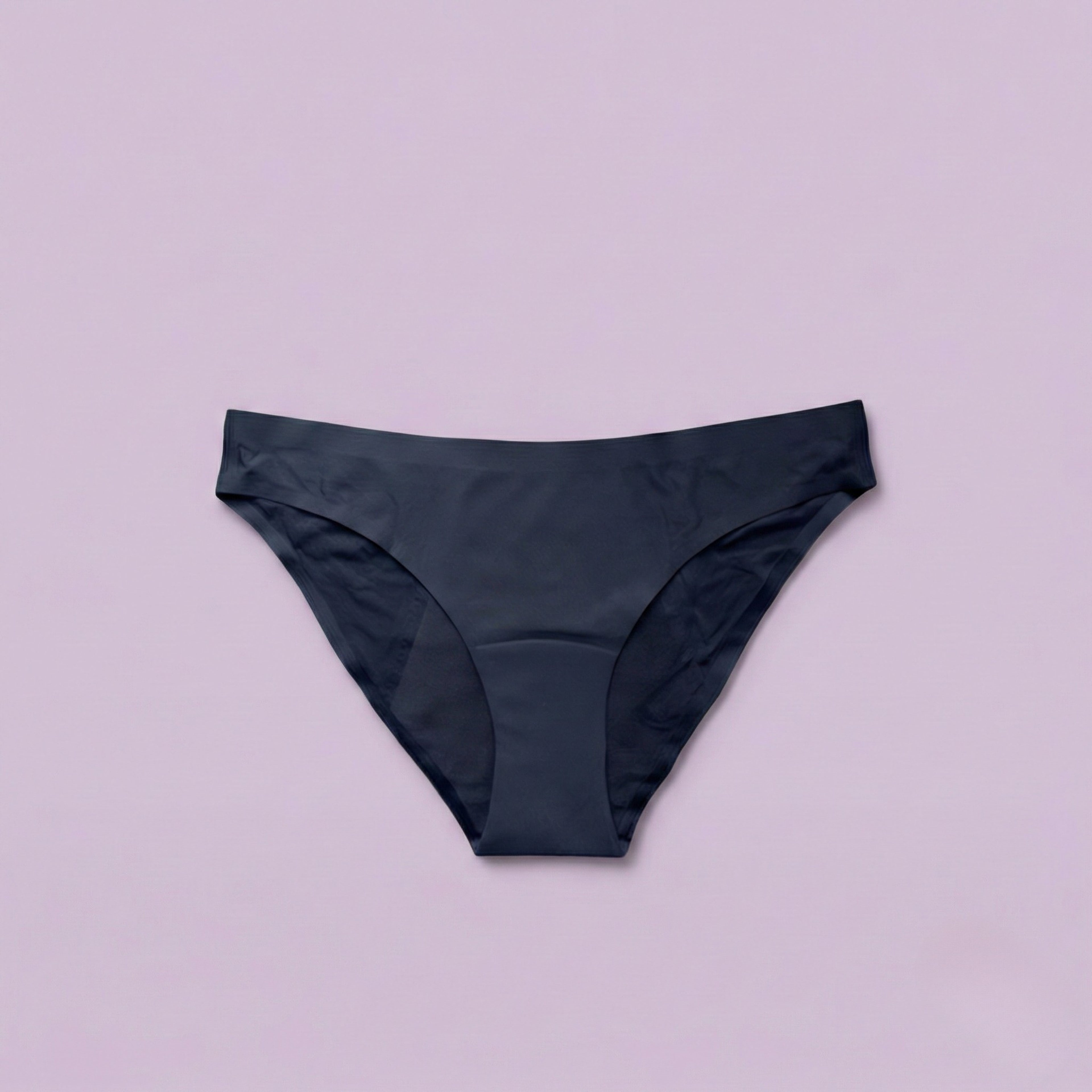 Braguita menstrual sin costuras Apparelle negra - producto plano sobre fondo rosa mostrando diseño bikini clásico