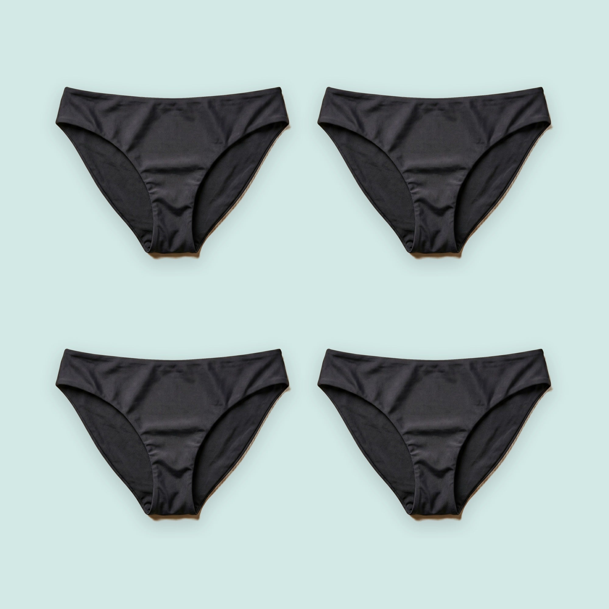 Pack de cuatro bikinis menstruales Apparelle en negro sobre fondo verde agua