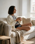 Mujer sentada en un sofá de lino con una taza, con braga menstrual de tiro alto Apparelle en negro